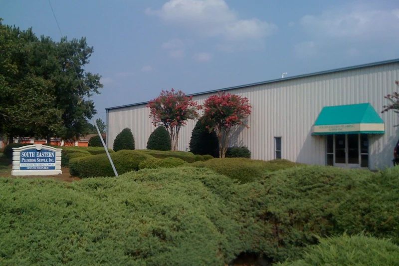 The South Eastern Plumbing Supply building on Veterans Parkway in 2010: a metal warehouse with a green awning over the door, behind low hedges and the company sign